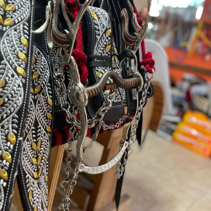 Engraved silver bit with chains hanging on an embroidered charro saddle