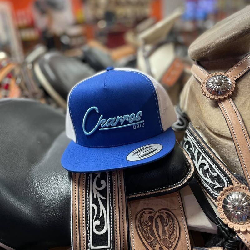 Blue and white Charros snapback cap resting on a tooled saddle
