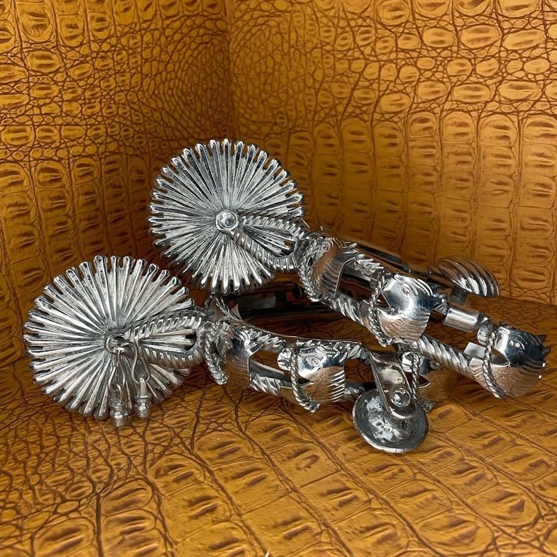Pair of polished silver charro spurs with large rowels on gator-print leather